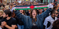 Eine Frau in einer Demonstration schreit, sie breitet einen schal aus, auf dem Palestine steht