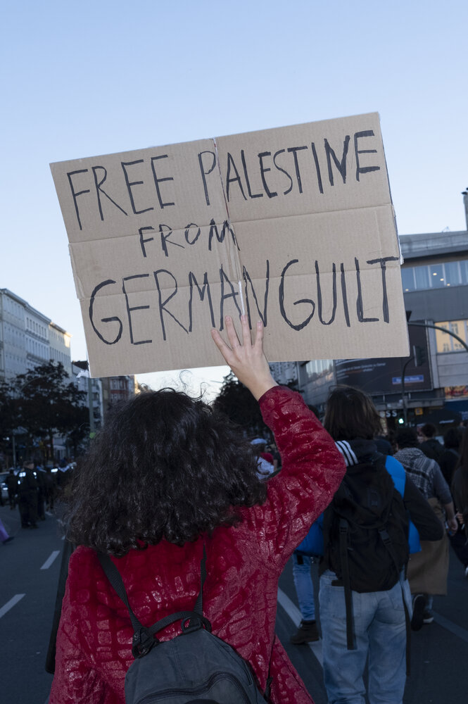 Eine Frau im roten Oberteil trägt ein Pappschild mit der Aufschrift "Free Palestine from german guilt"