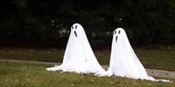 Zwei kleine Geister aus weißen Laken mit Geistergesicht in einem Park
