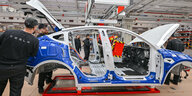Ein noch nicht fertigproduziertes Tesla-Fahrzeug in der Herstellungsstraße, Arbeiter machen sich an ihm zu schaffen