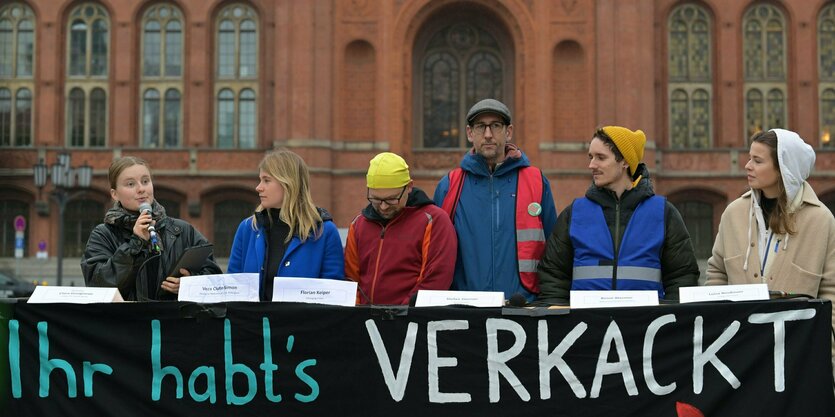 Aktivist:innen sprechen vor dem Roten Rathaus während einer Pressekonferenz von Fridays for Future zur Klima-Bilanz eines halben Jahres der schwarz-roten Koalition über dem Schriftzug "Ihr habt's verkackt".