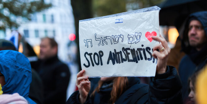 Eine Frau hält einen Zettel vor ihr Gesicht, darauf stehen die Worte "Stop Antisemitism", auch in Hebräisch