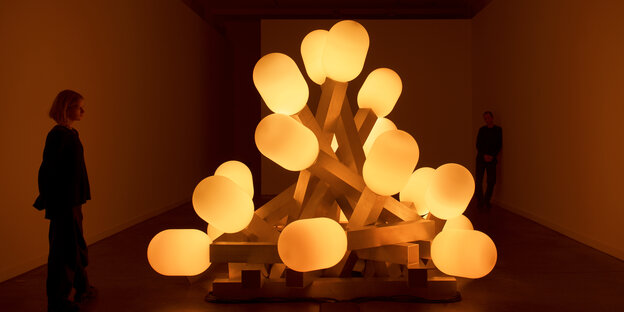 Ausstellungsbesucher betrachten eine Installation in Form einer Ansammlung gelber Lampen