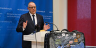 Innenminister Michael Stübgen spricht auf einer Pressekonferenz, vor ihm eine große, bemalte Tasche