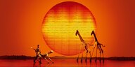 Zwei große Giraffen auf einer Bühne vor glühend roter Sonne: ein Szenenfoto aus dem Musical König der Löwen in Hamburg