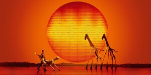 Zwei große Giraffen auf einer Bühne vor glühend roter Sonne: ein Szenenfoto aus dem Musical König der Löwen in Hamburg