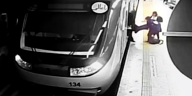 Ausschnitt einer unscharfen Videoaufnahme in einem U-Bahnhof. Man sieht wie eine junge Frau von zwei Personen aus einem im Bahnhof stehenden Zug getragen wird.