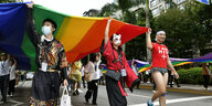 drei Menschen laufen auf einer Straße und halten eine Regenbogenflagge