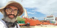 Ein Mann mit Hut vor einem ockerfarbenen Transportschiff