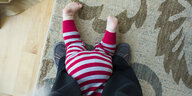 Ein Baby krabbelt zwischen den Füßen eines Erwachsenen.