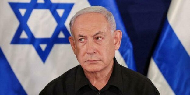 Benjamin Netanjahu guckt ernst drein. Im Hintergrund eine israelische Flagge
