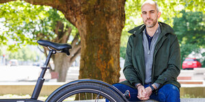 Hannovers Oberbürgermeister Belit Onay sitzt neben seinem Fahrrad vor einem Baum in Hannovers Innenstadt