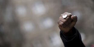 Eine gereckte Faust, am Mittelfinger ist ein Fingerring, der mit einem Detail in den Umrissen des afrikanischen KOntinents versehen ist