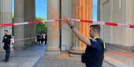 Polizist an einem Absperrband am ornage besprühten Brandenburger Tor