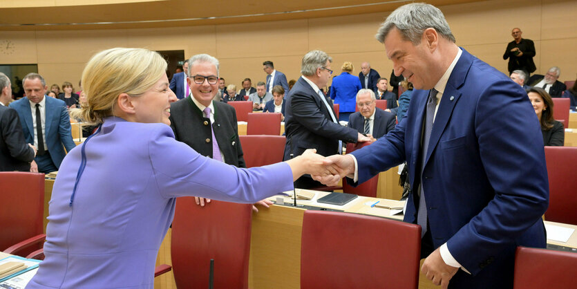 Schulze schüttelt Söders Hand im bayrischen Landtag, rote Stühle, Holzvertäfelung