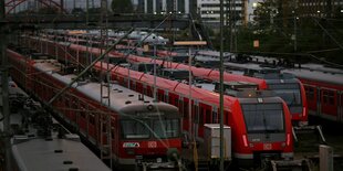 Rote Regionalzüge stehen auf mehreren Schienen nebeneinander in der Dämmerung.