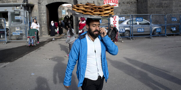 Ein Mann im leuchtend blauen Jackett trägt Brote auf dem Kopf
