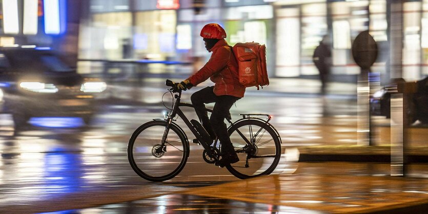 Ein Fahrradfahrer mit orangefarbenem Rucksack auf einer regennassen Strasse