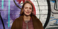 Portrait Ria Schroeder vor einer mit Graffiti vollgesprühten Mauer