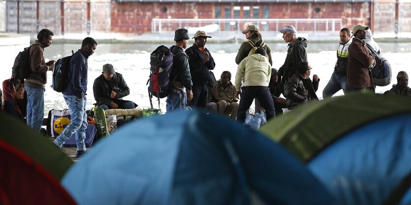 Menschen stehen im Flüchtlingslager vor Zelten.