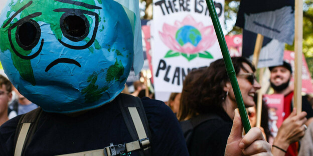Eine demonstrierende Person trägt einen traurig guckenden Globus als Maske über dem Kopf