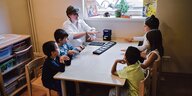 Fünf Kinder sitzen mit einer Lehrerin an einem Tisch am Fenster