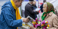Ein Mann steht einer älteren Frau auf der Straße gegenüber und gibt ihr eine Zeitung