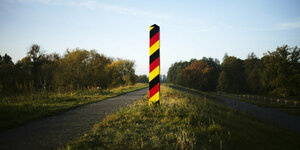 Ein Grenzpfahl in den deutschen Nationalfarben steht an einer Landstraße