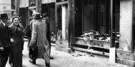 Menschen gehen die Straße entlang, manche lächeln, andere bleiben vor einem während des Pogroms von 1938 angegriffenen Geschäft stehen