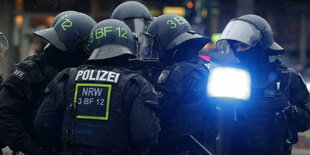 Mehrere Polizisten in Kampfmontur stehen dicht beieinander, im Vordergrund ein Licht, was bläulich leuchtet