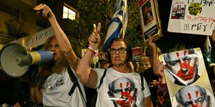 Demonstranten stehen vor der Residenz von Benjamin Nethanjahu und fordern seinen Rücktritt - sie tragen T-Shirts und Plakate mit einer roten Hand auf seinem Porträt