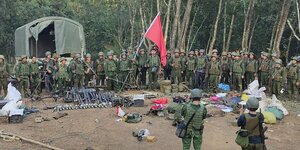Bewaffnete Rebellen präsentieren unter einer roten Fahne Waffen, die sie bei der Einnahme eines Militärpostens in Chinshwehaw nach eigenen Angaben erbeutet haben.