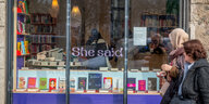 Schaufenster des Buchladens "SheSaid" in Berlin, Kreuzberg. Davor laufen zwei Frauen entlang, eine trägt Kopftuch