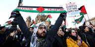 Ein junger Mann hält einen Schal mit dem Muster der palästinensische Flagge auf einer Demo in Berlin, umringt von Demonstranten die auch Falggen und Schilder hochhalten