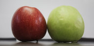 Ein roter und ein grüner Apfel liegen auf einem Tisch.