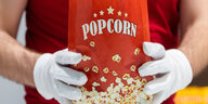 Ein Mitarbeiter eines Kinos hält Popcorn in den Händen.