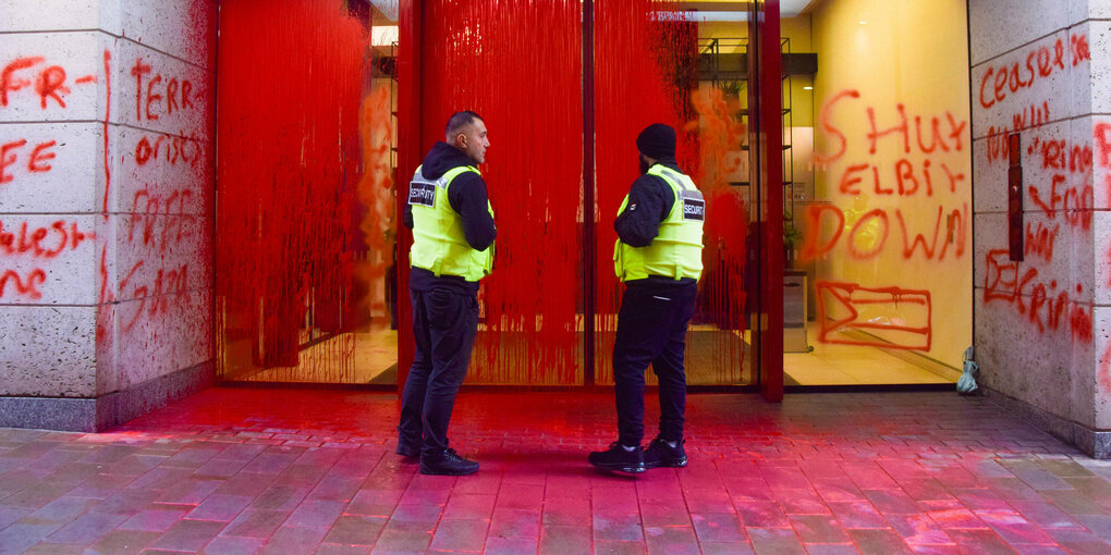 Zwei Polizisten vor dem mit roter Farbe bespritztem Eingang eines Gebäudes