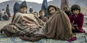 Aus Pakistan zurückgekehrte afghanische Flüchtlinge warten in Decken gehüllt auf einem Teppich unter freiem Himmel nahe dem Grenzübergang Torkham