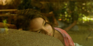Ein Mädchen liegt mit ihrem Kopf auf einem Sofa und schaut traurig