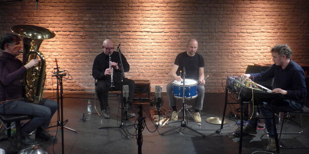 Das Quartett Werckmeister sitz auf eine Bühne, von links nach rechts sind die Musiker an der Tuba, mit Klarinette, am Schlagwerk und an einem Keyboard mit zahlreichhen Kabeln zu sehen.