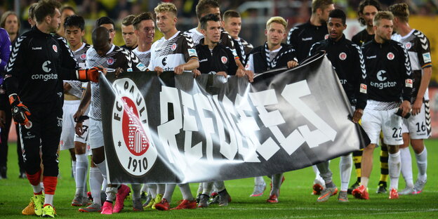 St. Pauli-Spieler halten ein Transparent mit der Aufschrift „Refugees“ hoch