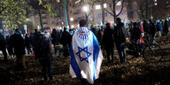 Eine Menschenmenge an einem dunklen Ort, eine Person der VVN ist in die Fahne Israels gehüllt
