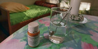 Ein Glas Wasser und ein Behälter mit Medizin auf einem Tisch