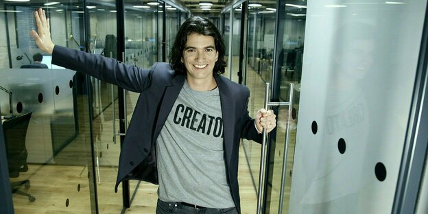 Der junge Adam Neumann lächelt einladend, trägt schulterlange, dunkle Haare, ein Sakko und darunter ein T-Shirt mit der Aufschrift: Creator