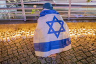 Eine Person wickelt sich in Israel-Flagge ein un kniet vor Kerzen