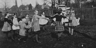Kinder tanzen in einem Kreis auf dem Schulhof - Schwarzweißfoto aus den 30er Jahren. Ilse Polak in der vorderen Reihe schaut in die Kamera