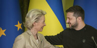 Ursula von der Leyen und Wolodymyr Selenskyj lächeln sich gut gelaunt an - hinter ihnen Flaggen in den Farben der Ukraine und Europas