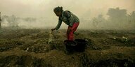Eine Frau gießt mit einer durchlöcherten Plastikflasche während eines Waldbrandes ihr Feld.