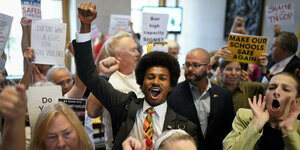 Eine Gruppe von Demonstranten, in ihrer Mitte ein junger schwarzer Mann, hält Schilder hoch und reckt Fäuste