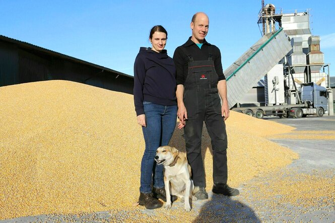 Clara und Moritz Stamm stehen mit ihrem Hund neben einem großen Haufen Maiskörner auf ihrem Hof